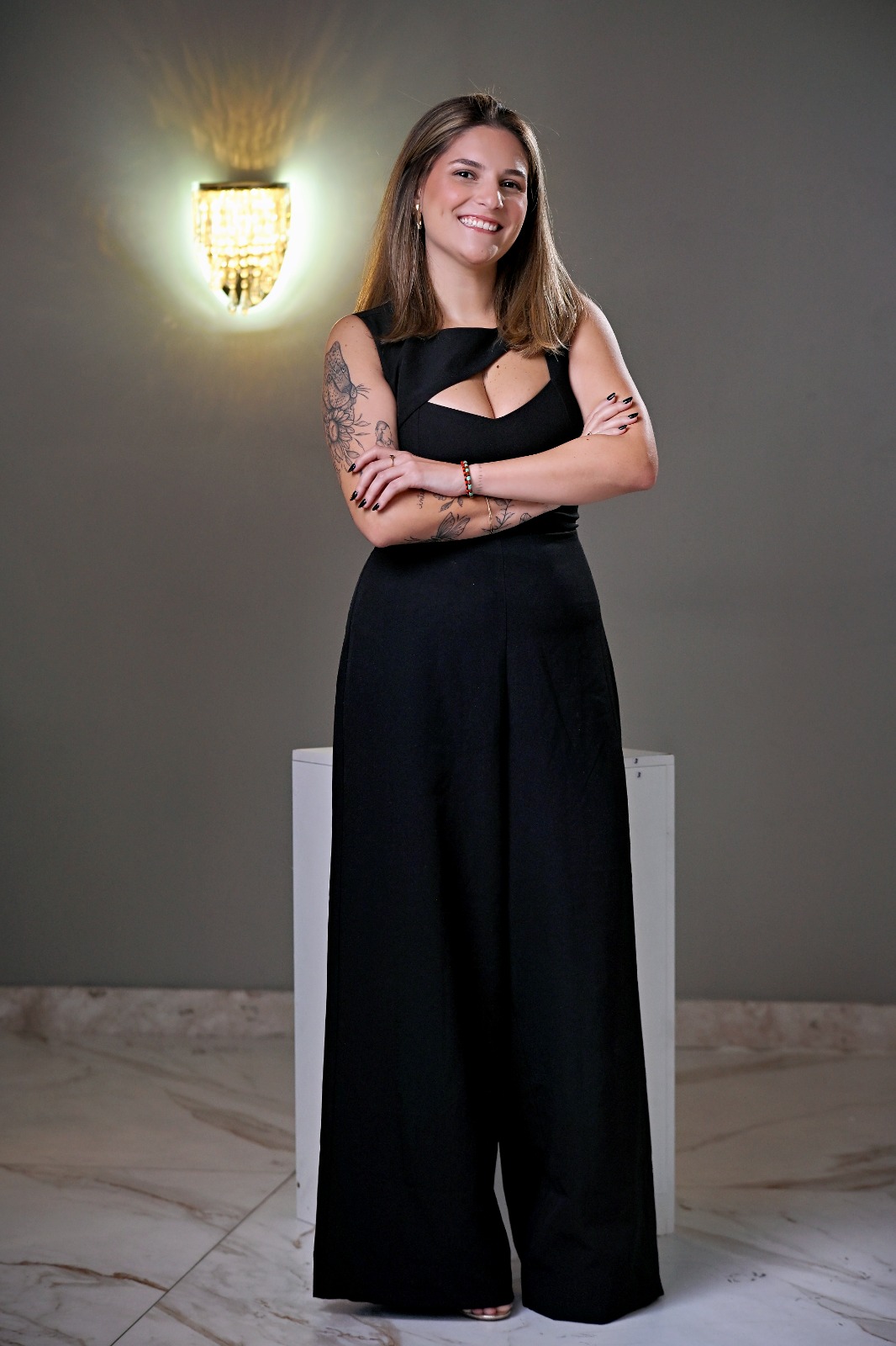 Carol sorrindo, em pé, de corpo inteiro